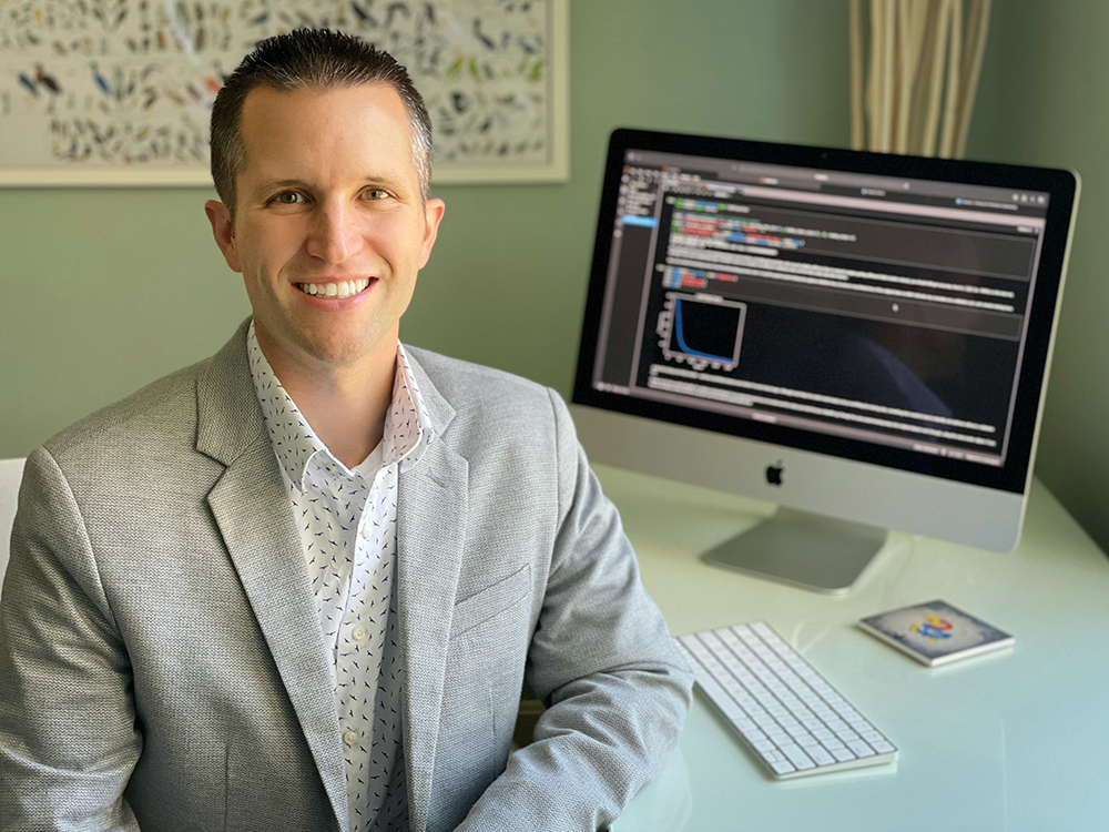 kevin leonard sitting at his desk with a computer screen filled with data in the background