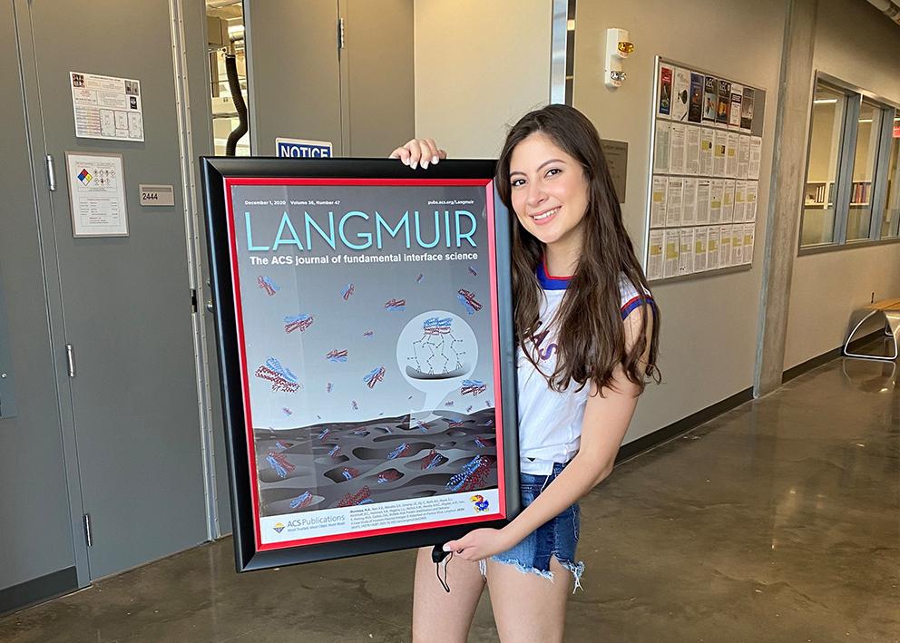 Grad student Nicole Montoya holding a framed copy of her first authored journal featured on Langmuir