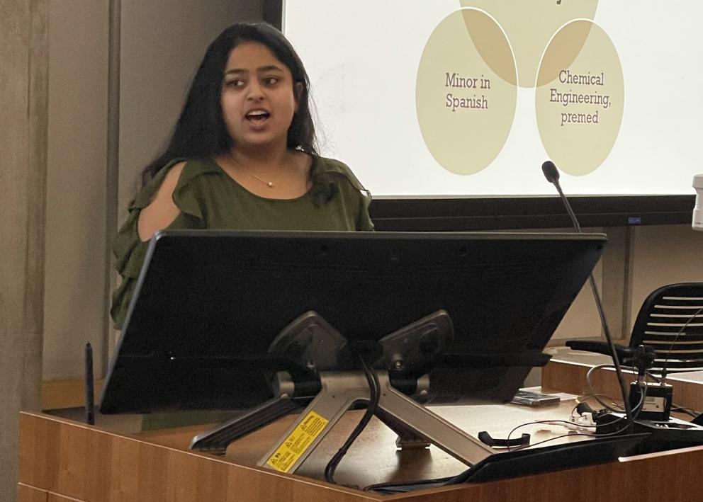 Student presenting at podium with powerpoint slide in background
