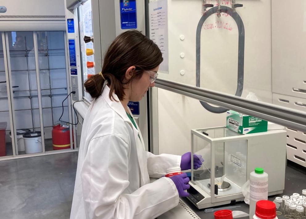 Student weighing chemicals in a fume hood in the lab