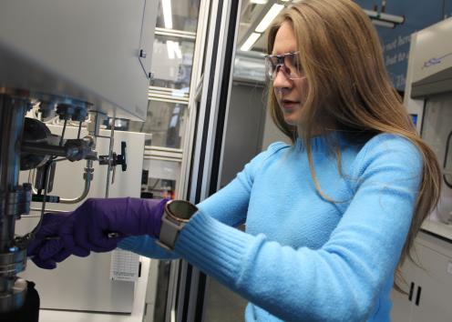 A student with gloves and goggles works with a piece of equipment