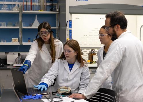four students in lab coats working on a project together