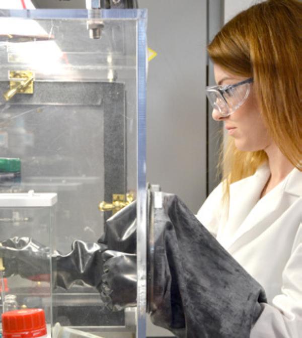 a student works with materials behind a protective shield