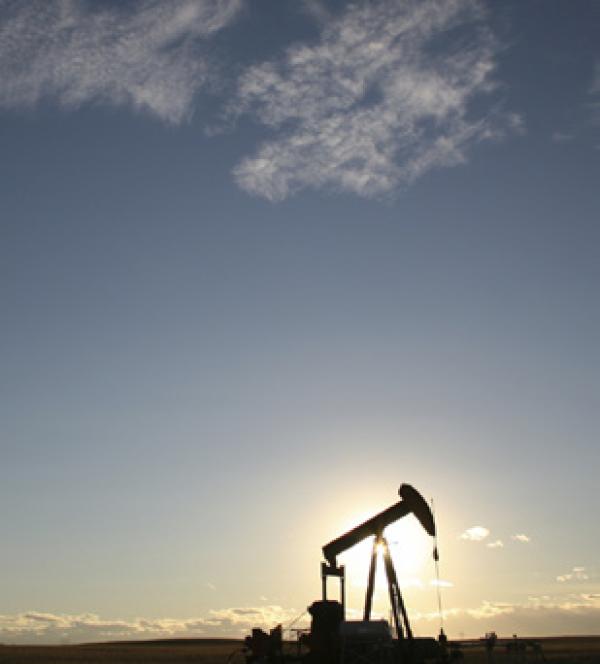 an oil derrick with the sun behind it