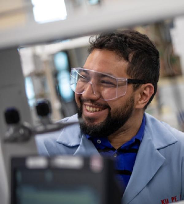 a researcher wearing goggles and smiling in a lab